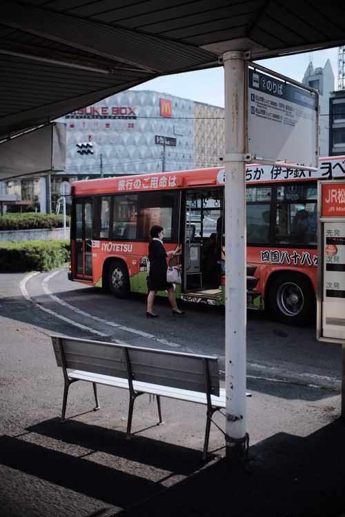 Free Urban scene of a woman boarding a bus at a bus stop on a sunny day. Stock Photo
