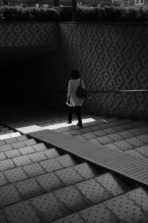 Free A solitary figure descends shadowy stairs in an urban setting, captured artistically in black and white. Stock Photo