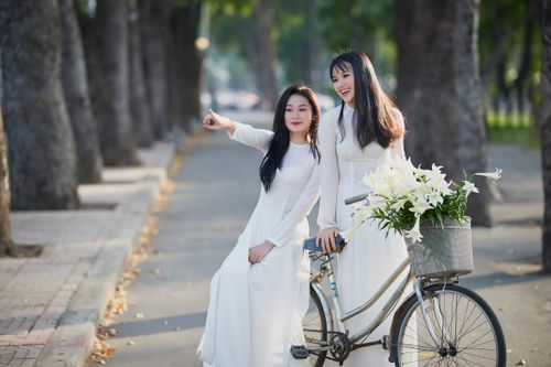 Free Two young women in white dresses posing with a bicycle in a sunny park setting. Stock Photo