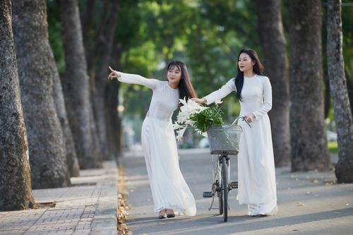 Free Two Asian women in white dresses walking with a bicycle in a park scene. Stock Photo