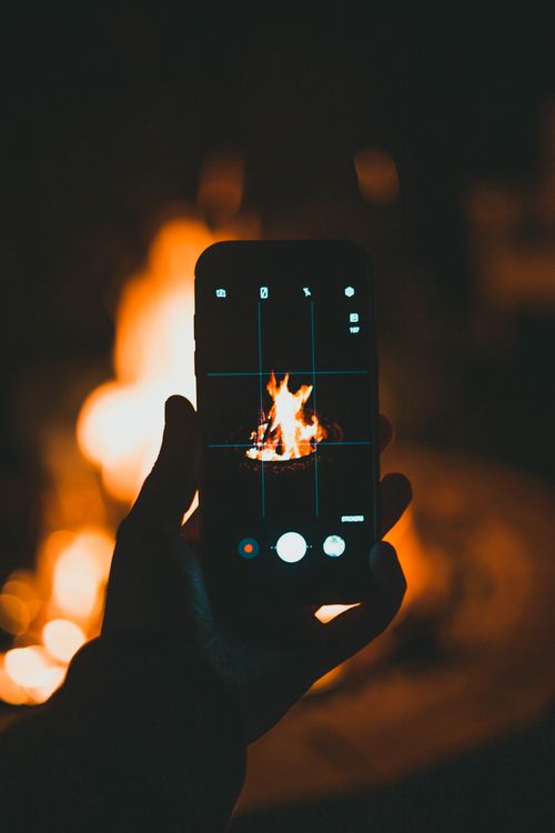 Free A smartphone captures a warm campfire blaze under a night sky, creating a contrast between technology and nature. Stock Photo