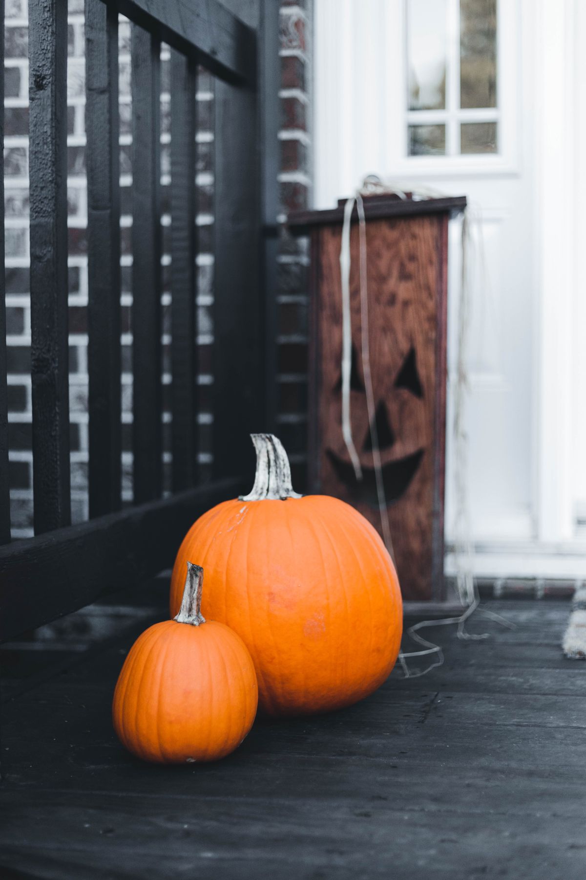 Two pumpkins on a porch with a spooky wooden jack-o'-lantern, creating a Halloween vibe. Stock Photo.
