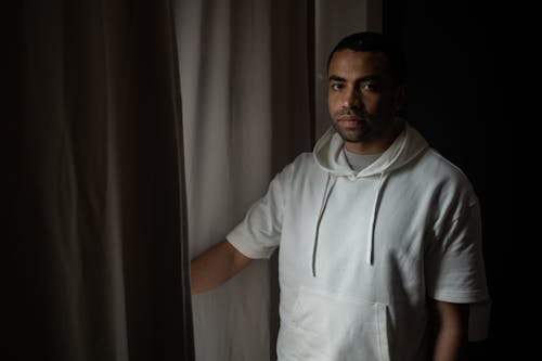 Man Wearing White Hoodie Standing Beside the Window