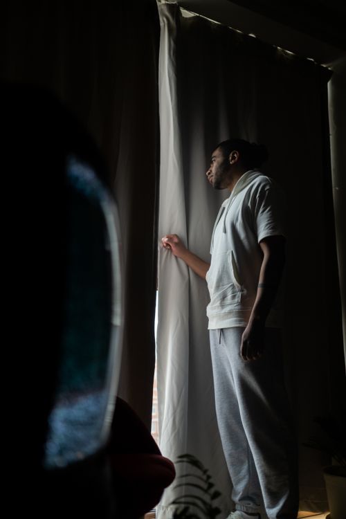 Free A man stands by a window, looking pensively outside, creating a mood of contemplation. Stock Photo