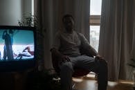 Man Sitting on a Chair at Home with TV on