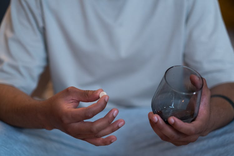 Person Taking A Pill And Holding Glass