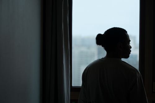 Free Silhouette of a man with ponytail gazing through a window with a blurred cityscape view. Stock Photo