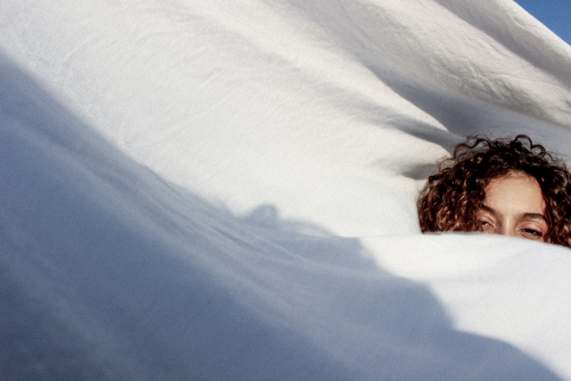 A woman peeks from under soft white sheets, enjoying a peaceful moment.