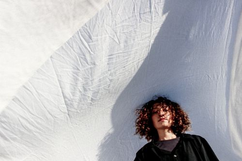 Free A young person with curly hair is framed against a backdrop of flowing white fabric, captured from a low angle. Stock Photo