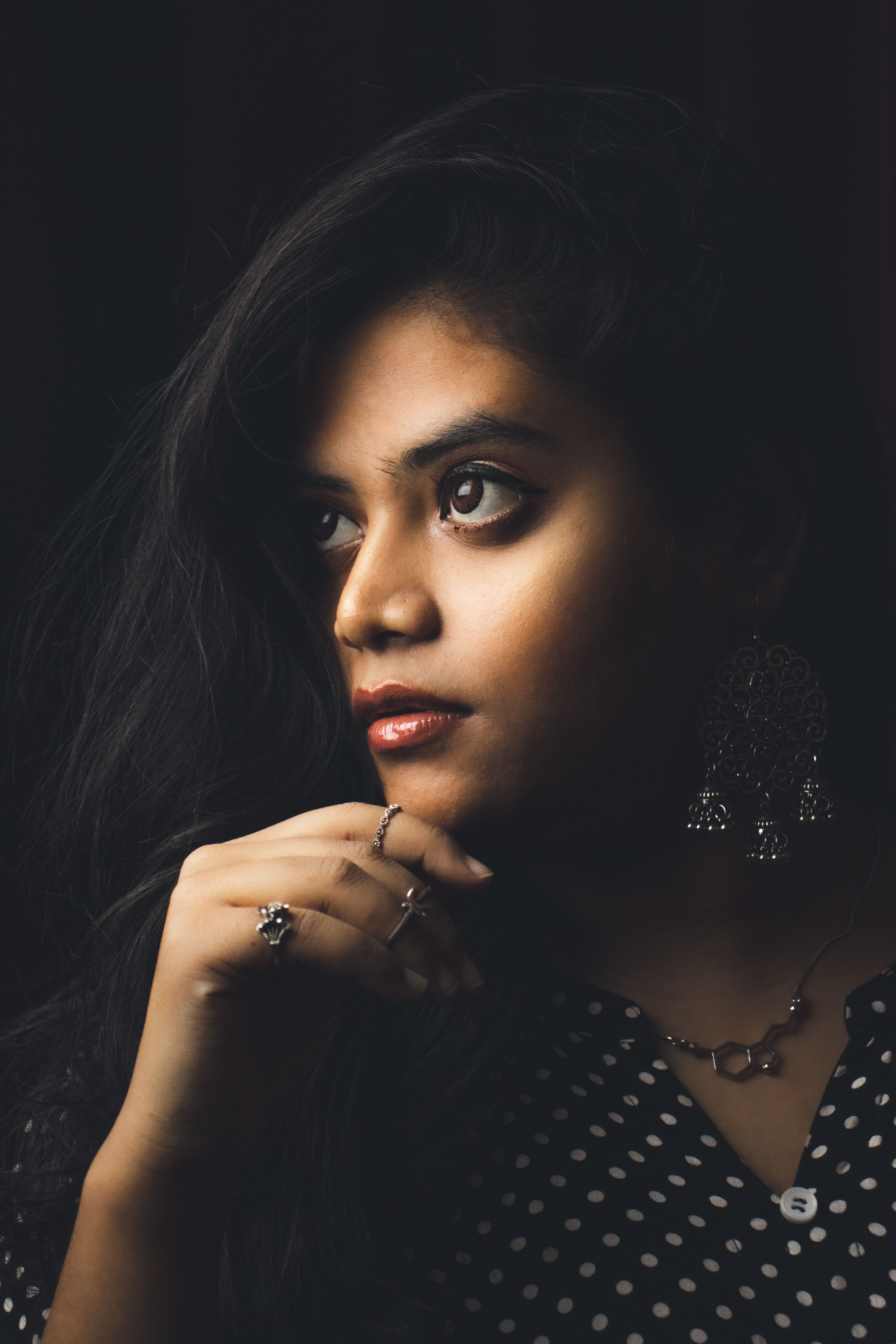 Close-up portrait of a thoughtful woman in jewelry with hand on chin pose, dim lighting.