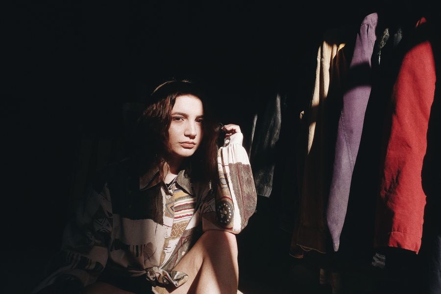 Artistic portrait of a woman sitting in sunlight with vibrant clothing around.