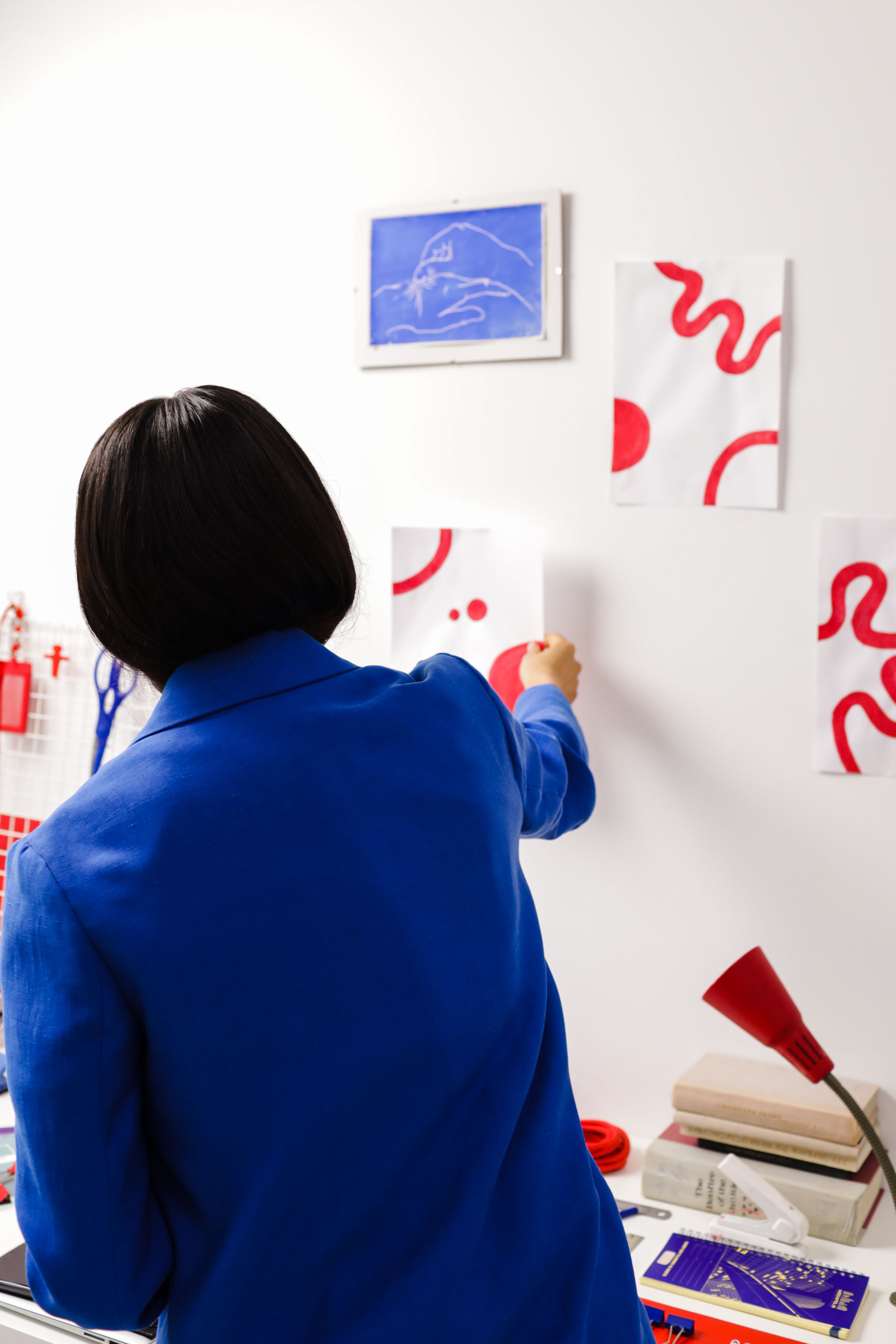 Rear view of woman hanging abstract art on wall in a modern creative workspace.