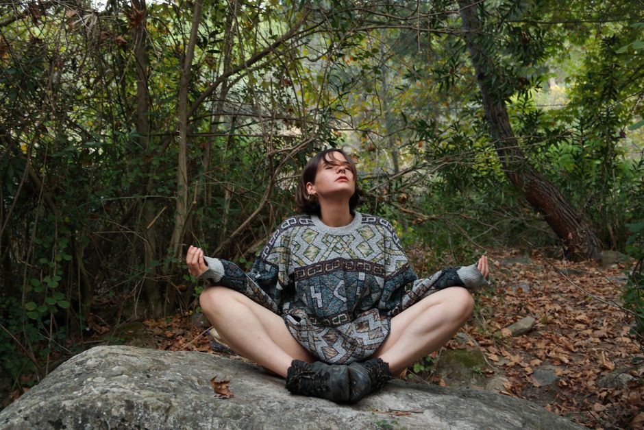 Person meditating on a rock in a peaceful forest — mindfulness and stillness