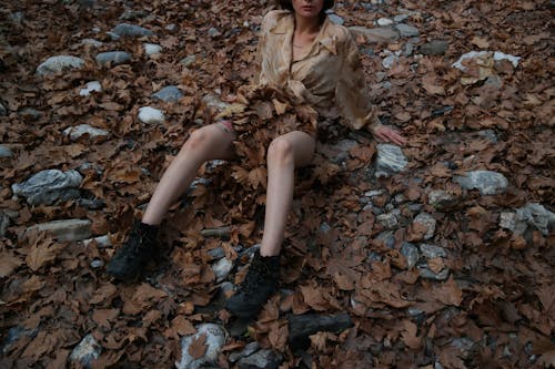 Photo of a Woman in a Brown Shirt Sitting on the Ground with Brown Leaves