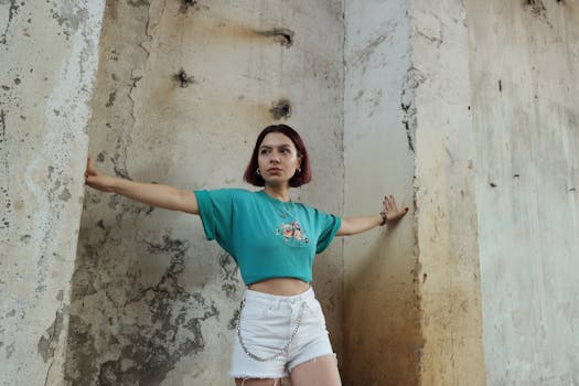 Stylish woman posing confidently against a textured urban wall in a crop top and shorts.
