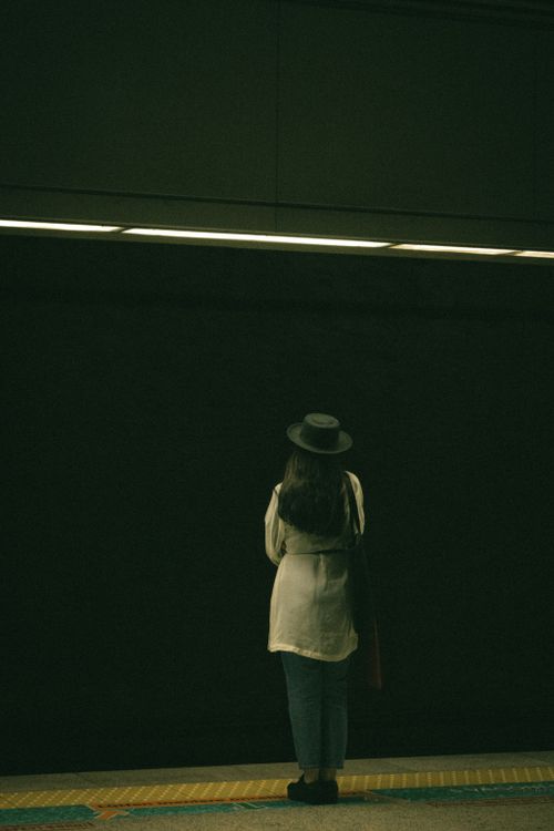 Free A woman stands alone at a subway station, wearing a fedora, captured from behind. Stock Photo