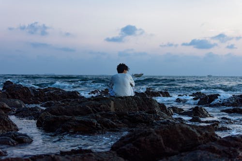 Free A Man Sitting on the Rocks Near a Body of Water Stock Photo