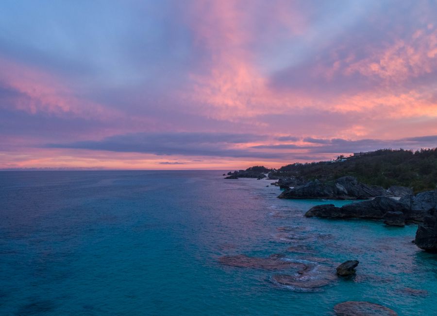 Captivating sunset over Bermuda's rocky coastline with vivid skies and tranquil sea.