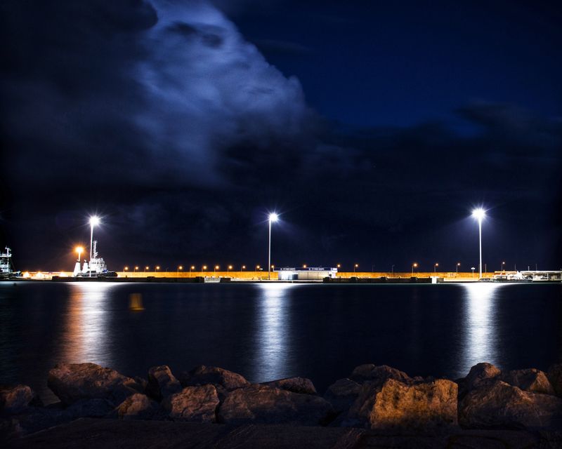 A long pier of streetlights reflecting on still water after dusk — photo by Kostas Dimopoulos on Pexels