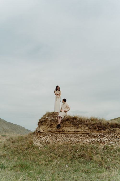 Free Two women elegantly pose on a grassy cliff, showcasing a picturesque and adventurous landscape. Stock Photo