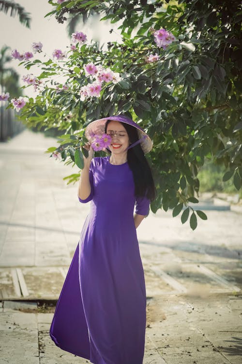 Free A Woman in Purple Dress Holding Purple Flowers Stock Photo