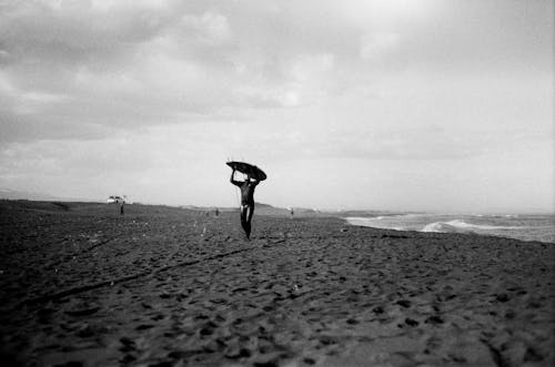 Grayscale Photo of a Person Carrying Surfboard