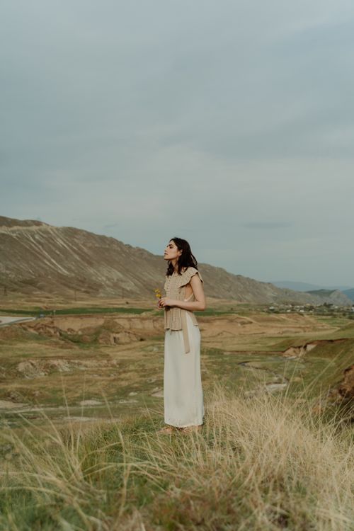 Free Elegantly dressed woman standing in a tranquil grassy landscape, embracing nature's beauty. Stock Photo