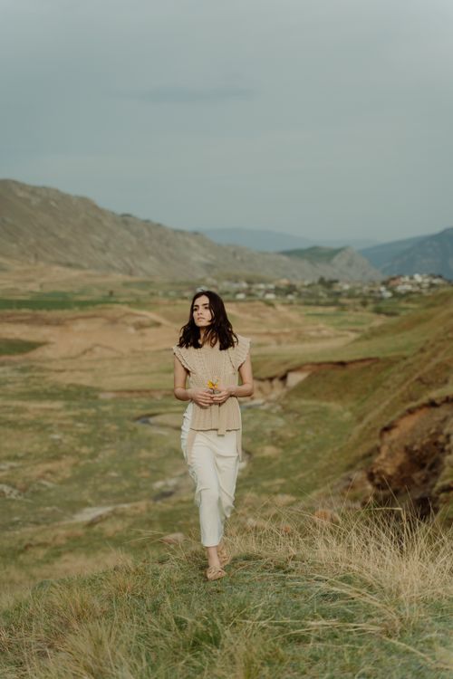 Free A serene scene of a woman walking through a rural meadow, holding flowers. Stock Photo