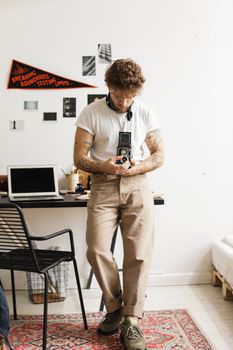 Man with tattoos using a vintage camera in a cozy home office setting.
