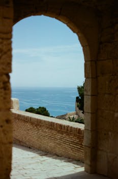 A stunning Mediterranean view captured through a historic stone archway in Alicante, Spain.