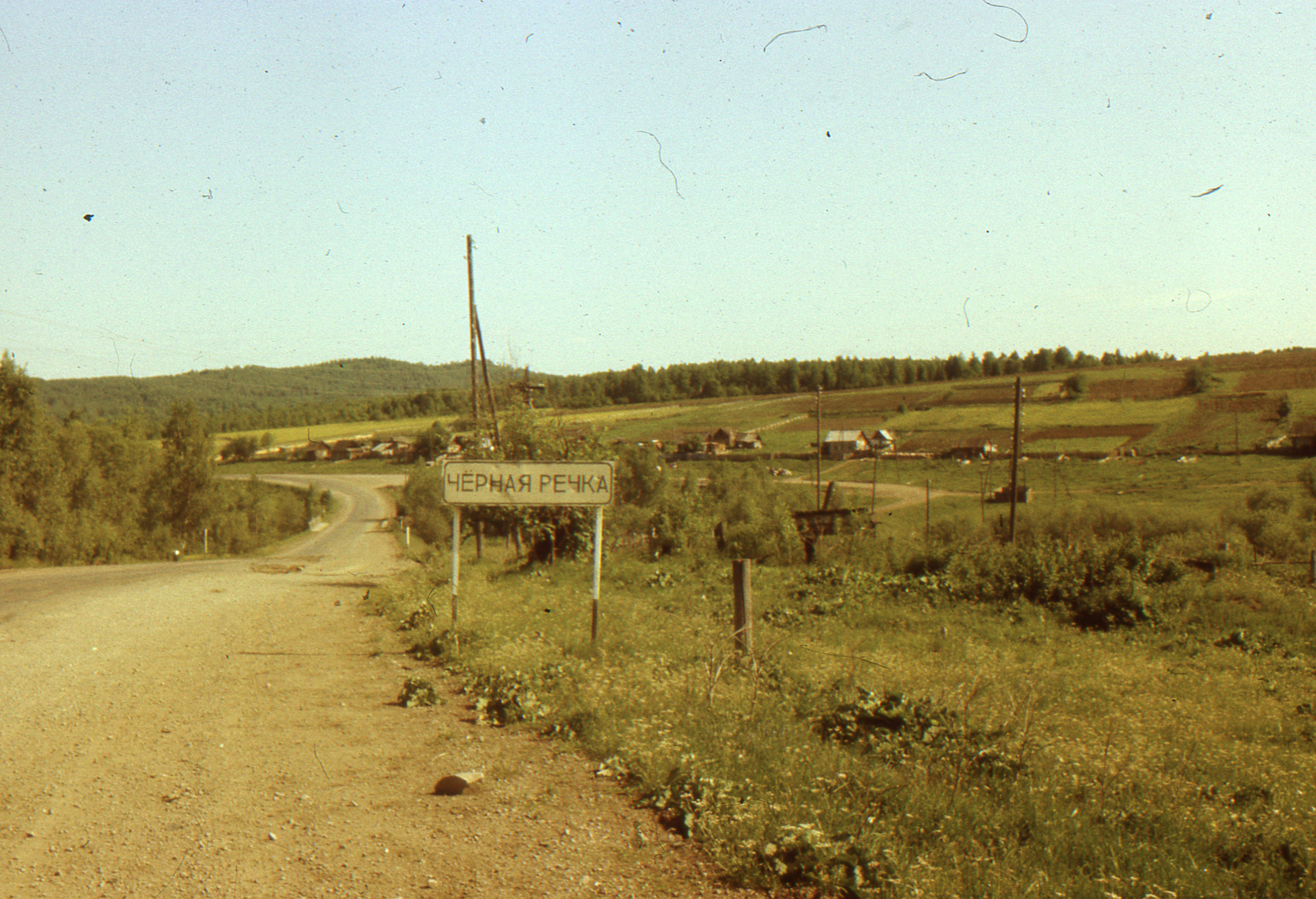 Scenic rural road and countryside with Chernaia Rechka sign under clear skies.