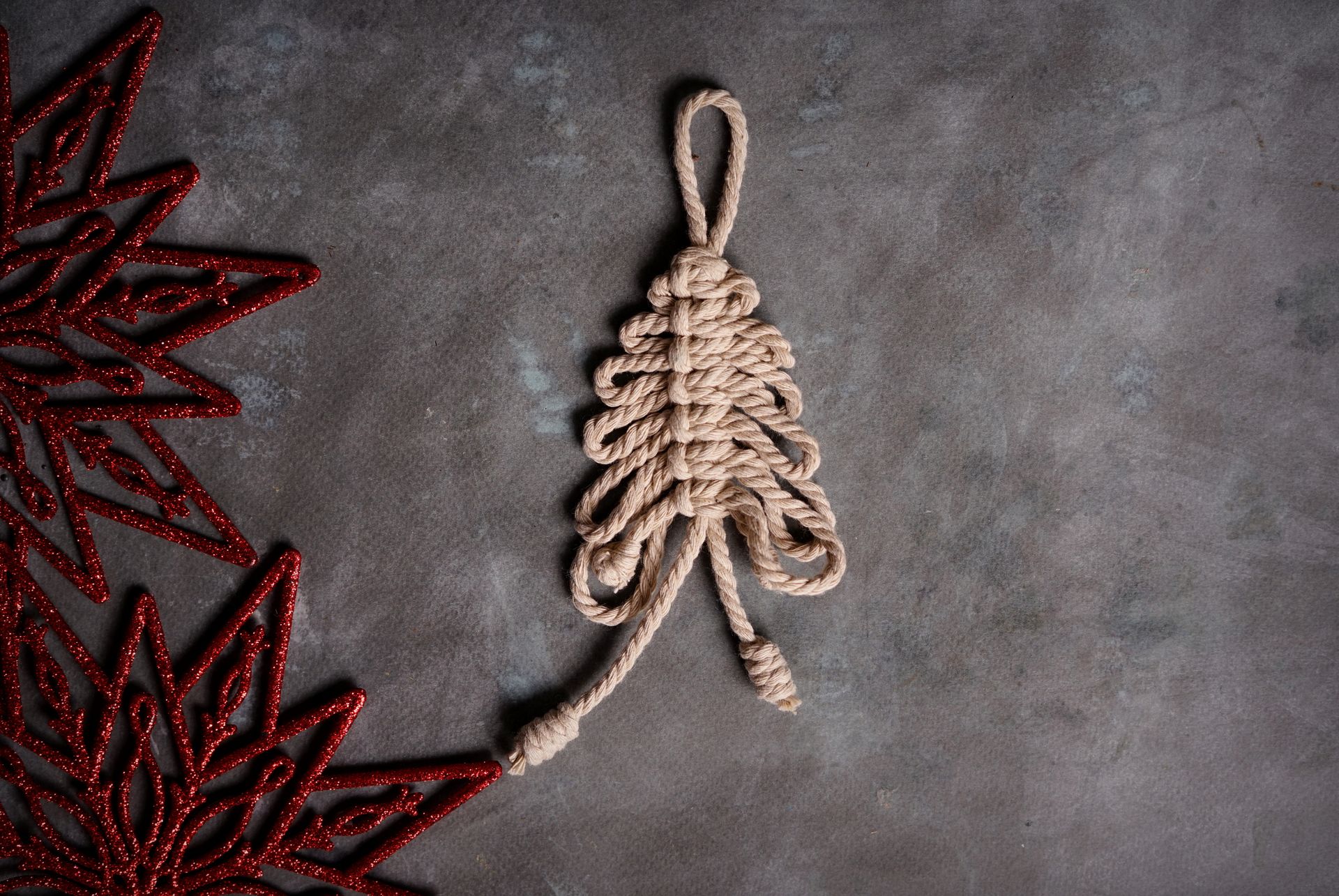 Artistic handmade rope Christmas tree with red decorations laid on a gray surface, perfect for holiday themes.