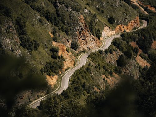 Free Scenic aerial view of a winding road cutting through a lush mountainside with trees and rocky terrain. Stock Photo