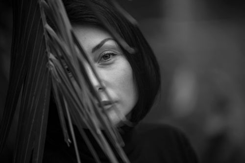 Free Artistic black and white portrait of a woman partially obscured by leaves, creating a mysterious look. Stock Photo