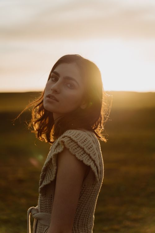 Free A thoughtful portrait of a young woman standing in a sunlit field at dusk. Stock Photo
