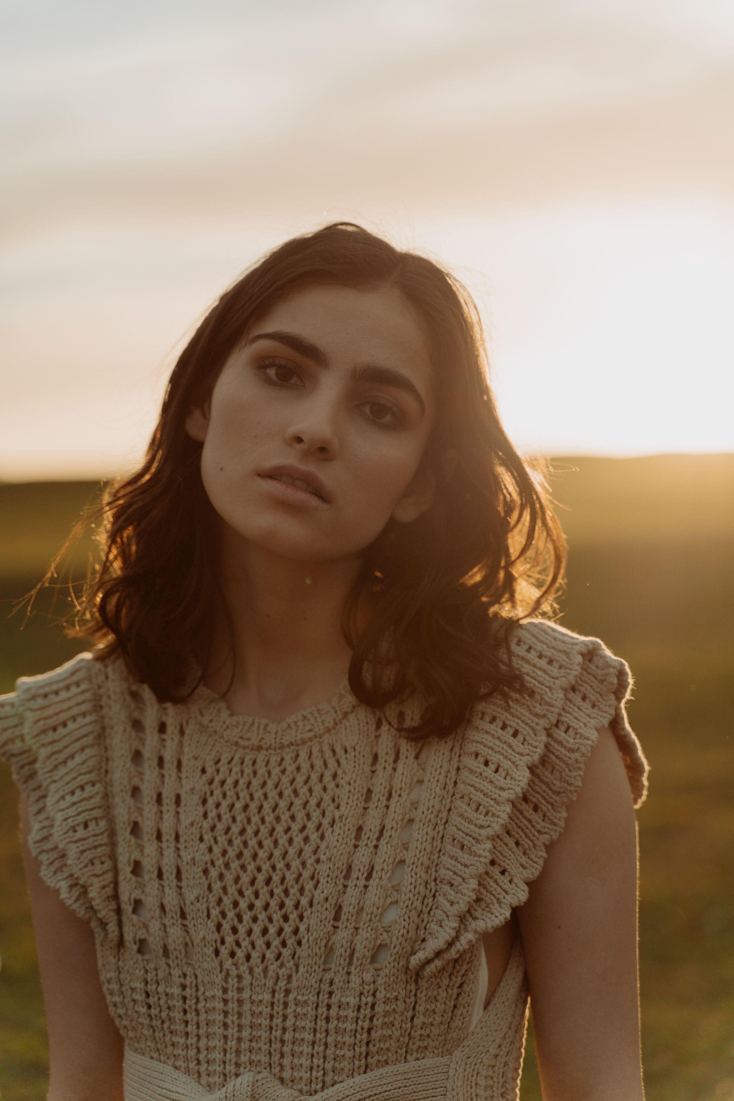 A portrait of a woman in a knitted top at sunset, showcasing natural beauty.