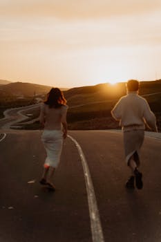 Two people running on a winding road at sunset, enjoying the golden hour outdoors.