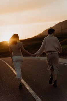 Two women walking hand in hand during sunset on a quiet road.