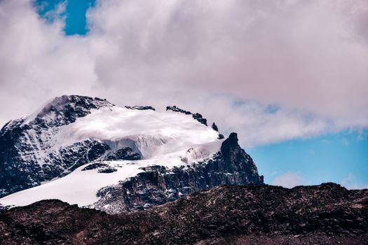 Majestic snow-covered mountain peak with rugged rock faces under a cloudy sky, perfect for nature and travel themes.