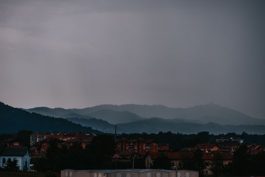 Cityscape under a heavy overcast sky, bordered by layered hills creating a dramatic visual.