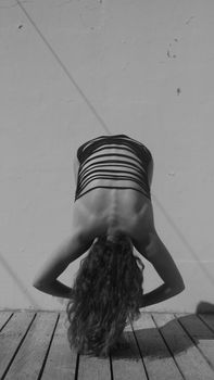 Monochrome photo of a woman in a swimsuit performing an artistic yoga pose outdoors.