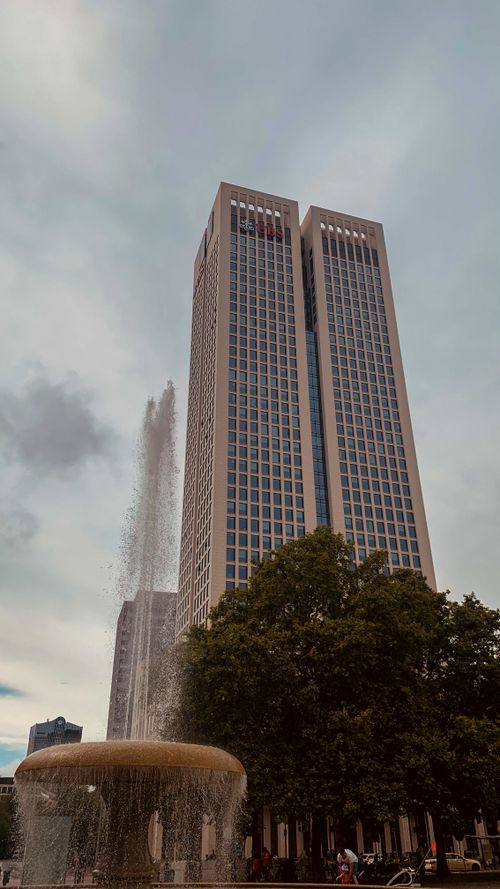 Free Modern skyscraper with a fountain in an urban downtown setting, amid trees. Stock Photo