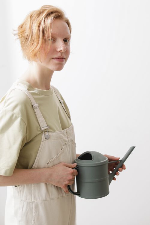 Free Woman posing with a green watering can against a white background, wearing light overalls. Stock Photo