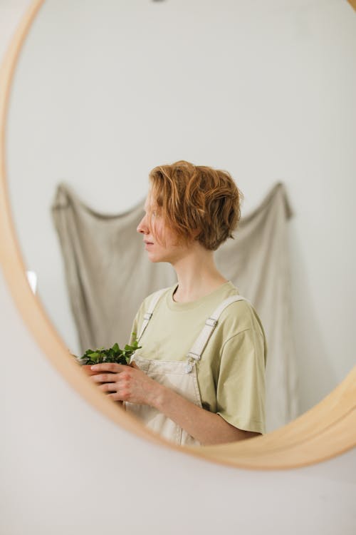 Reflection of a Woman Looking Afar While Holding a Plotted Plant