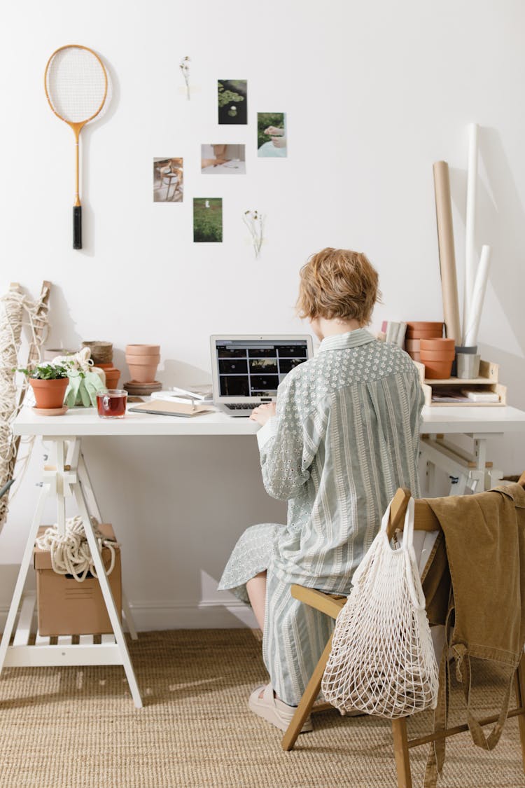 Back View Shot Of A Woman Sitting On A Wooden Chair While Working On A Laptop