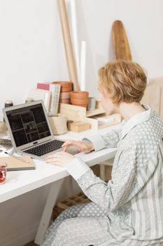 A young adult woman working remotely from home with a laptop in a cozy workspace.