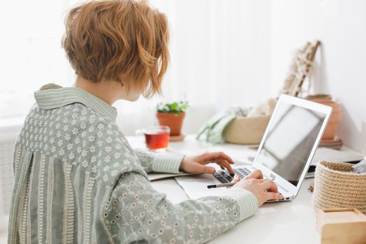 A woman working remotely in a bright, minimalist home office with a laptop.