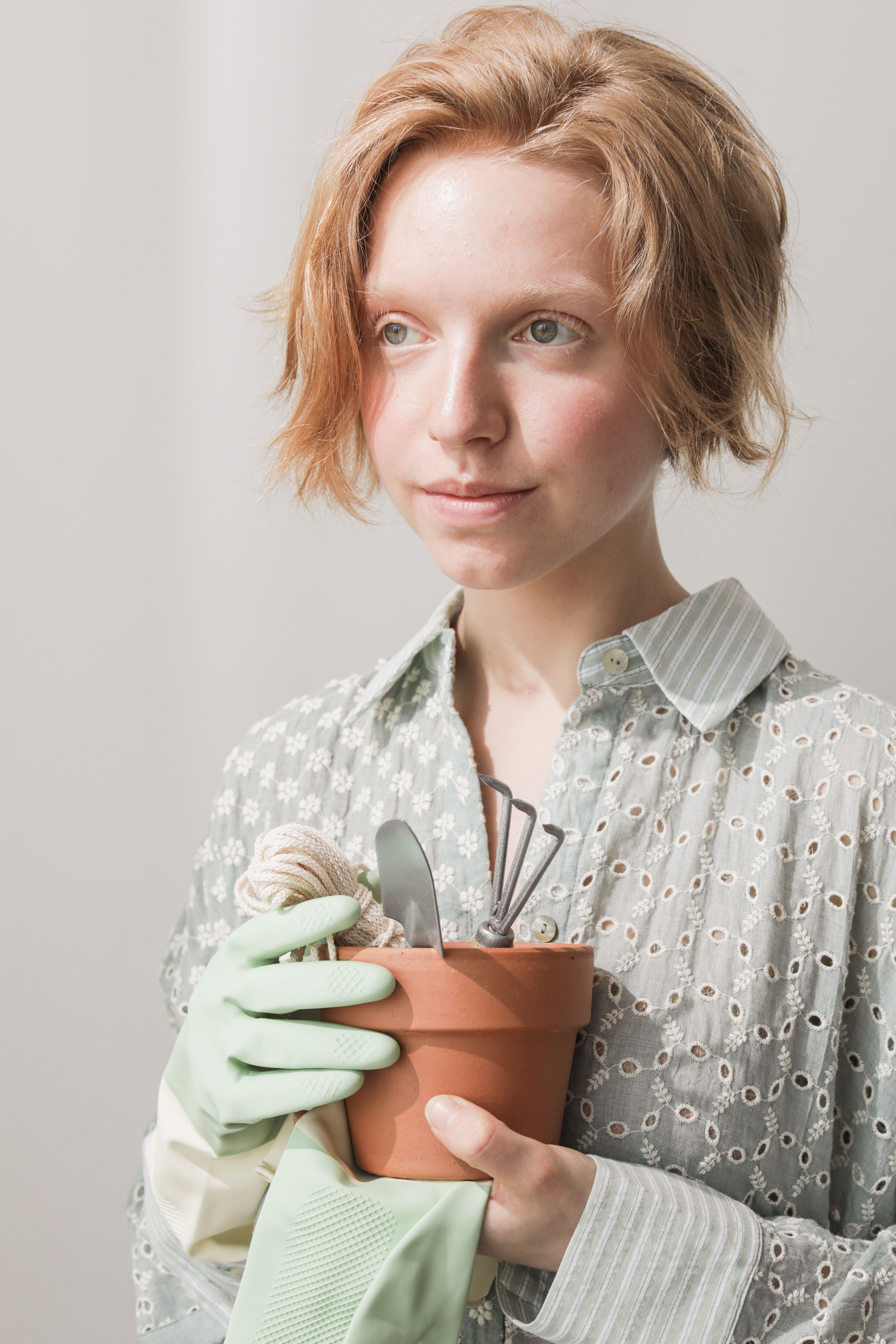 Portrait of a redhead woman with gardening gloves holding a potted plant indoors.