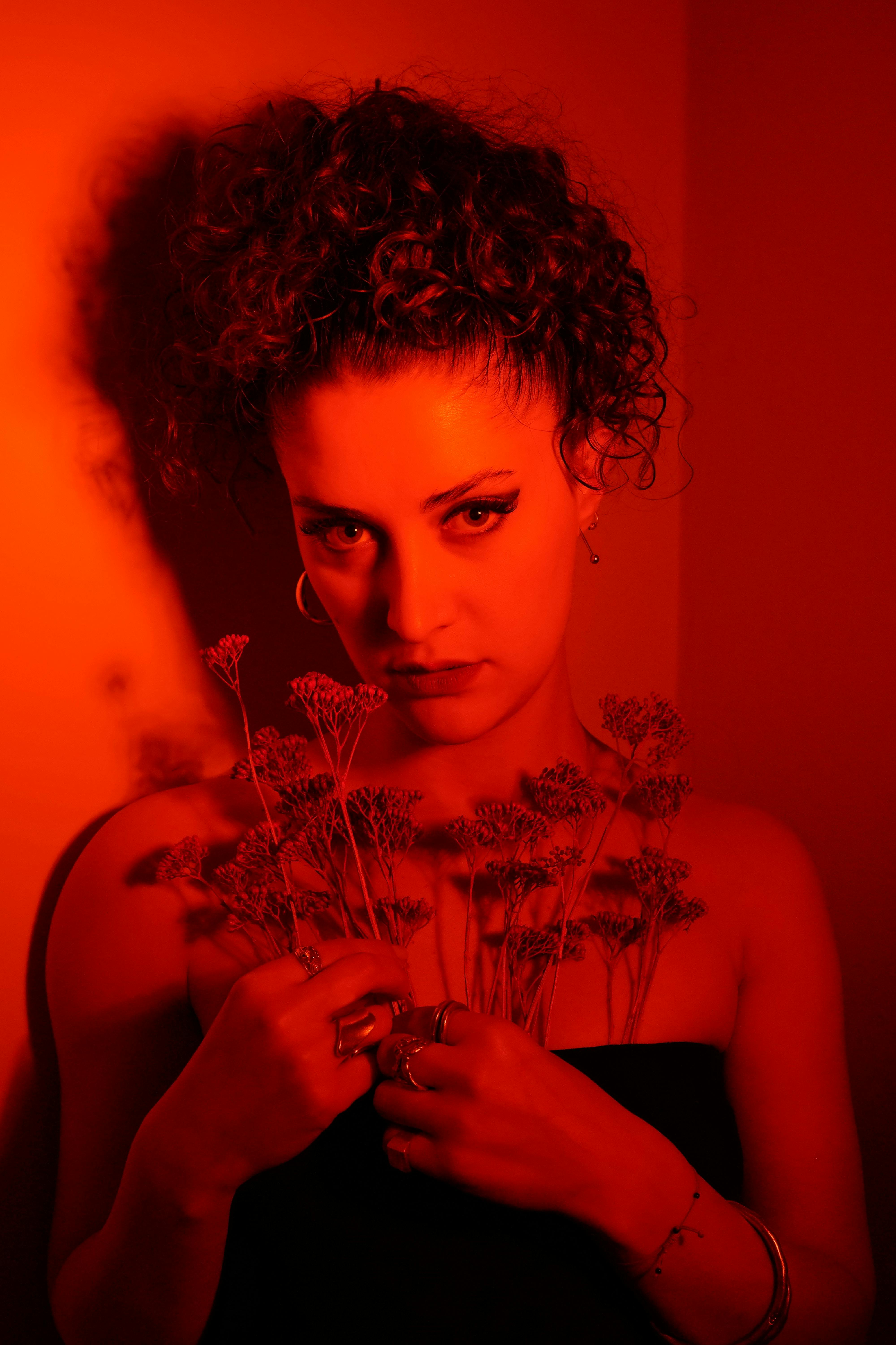 A dramatic portrait of a woman holding flowers with striking red lighting, creating a moody atmosphere.