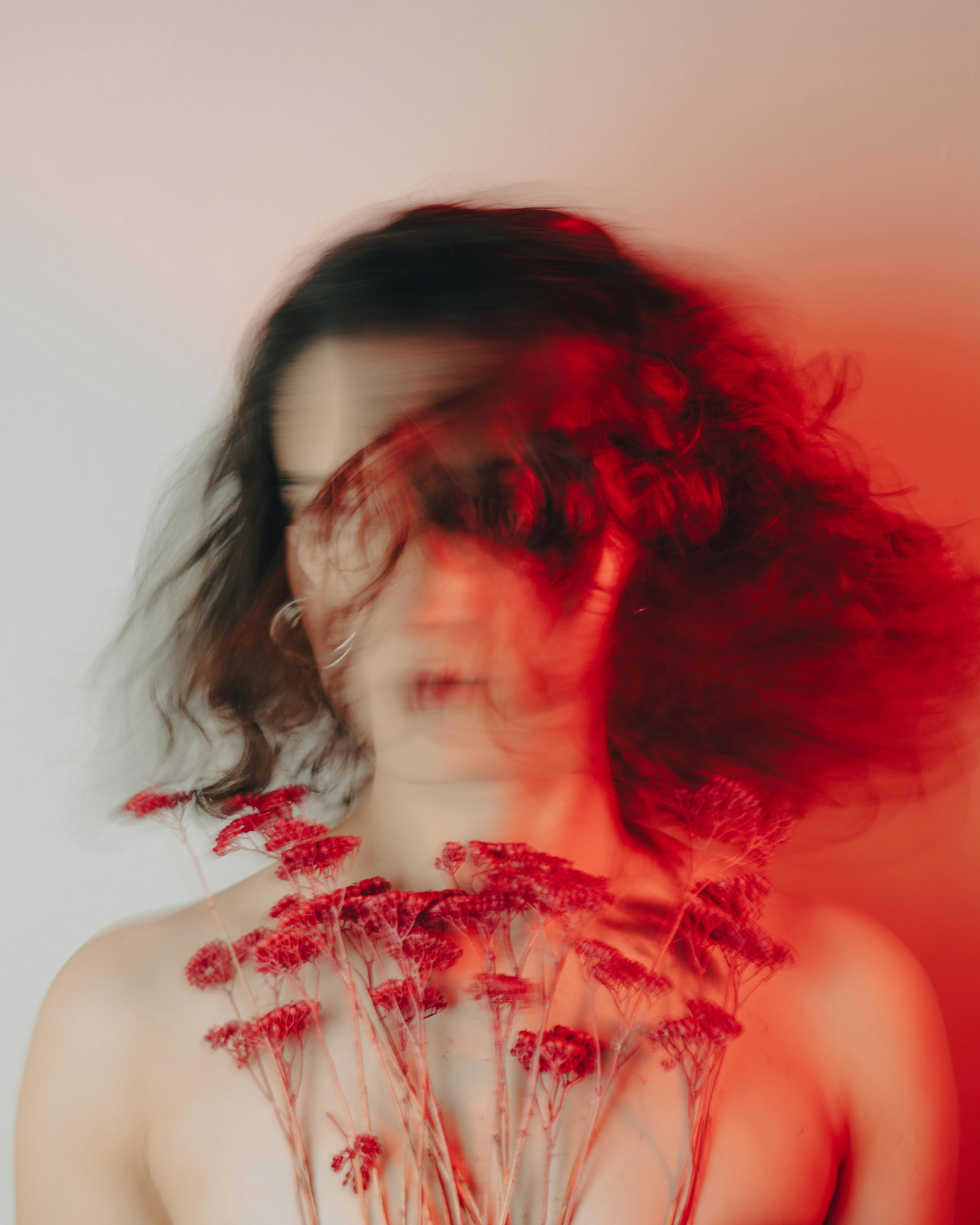 Creative blurred portrait of a woman holding red flowers, featuring artistic motion blur and vibrant red hues.
